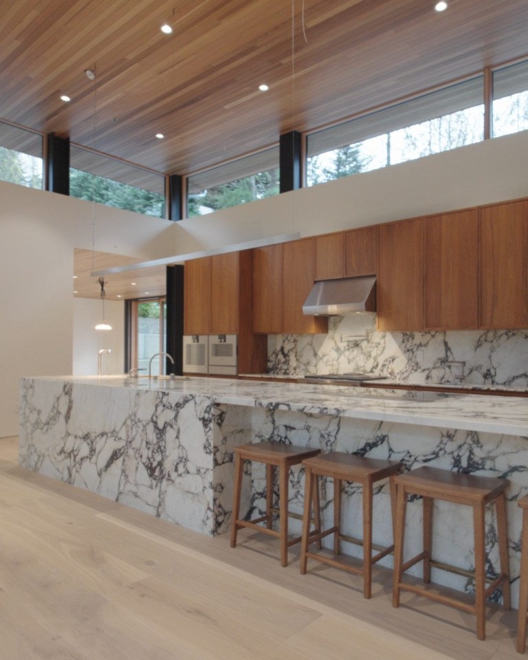 A long marble kitchen island with bold dark veining and wooden stools, fabricated by Allied Marble & Granite.